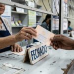 Bilhete da Loteria Federal sendo devolvido no balcão de uma lotérica fechada, com placa de fechado à mostra